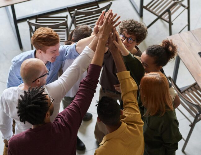 A diverse group of professionals high-fiving in a modern office, showcasing teamwork and collaboration.